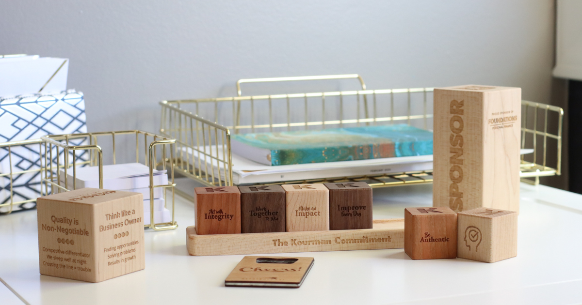 Collection of Smiling Tree Gifts wooden products engraved with company logos and phrases. Includes bottle opener, award blocks, and core value block and tray display.